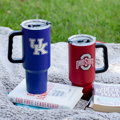 Two 40oz tumblers on a blanket in the grass with various books.